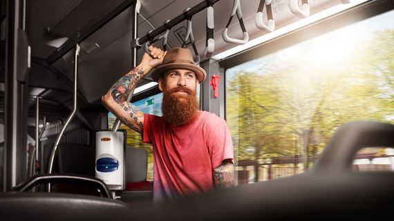 Zum Artikel Ein junger Mann mit Hut fährt in einem Bus und hält sich an einem Haltegriff fest