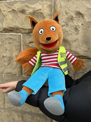 Eine Handpuppe, die eine gelbe Weste mit der Aufschrift Verkehrswacht trägt Eine Handpuppe, die eine gelbe Weste mit der Aufschrift Verkehrswacht trägt