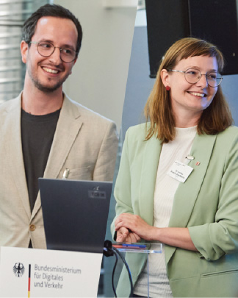 Dr. Annika Busch-Geertsema vom Hessischen Ministerium für Wirtschaft, Energie, Verkehr und Wohnen, und Jan Stübner von der HTAI GmbH, sprechen auf der 6. NaKoMo-Jahreskonferenz über nachhaltige Mobilitätspläne und Unterstützungsmaßnahmen in Hessen.